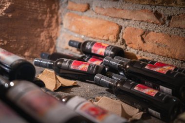 Taş bir yüzeyde kırmızı etiketli şarap şişelerinin toplanması, Ischgl, Avusturya 'da bir şarap mahzenini işaret eden, sıcak ışıkta tuğladan bir duvara dayanıyor..