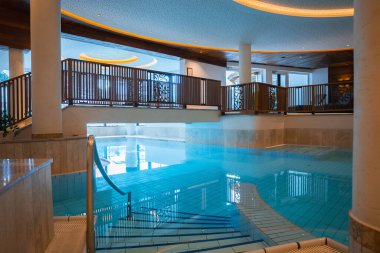 Modern kapalı havuz fayanslı döşeme, metal tırabzan, ahşap balkon, tenha aydınlatma ve Avusturya 'nın Ischgl kentinde lüks bir otelde büyük pencereler..