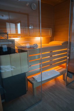 Parlak ahşap kaplamalı lüks sauna odası, cam muhafaza, çevre aydınlatması ve Avusturya 'nın Ischgl kentindeki üst düzey bir tesise düzgünce yerleştirilmiş havlular..