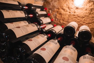 Yatay olarak istiflenmiş Tignanello şarap şişeleri sıcak, yumuşak aydınlatılmış bir şarap mahzeninde, dokulu bir duvarla, lüks bir ortam öneriyor..