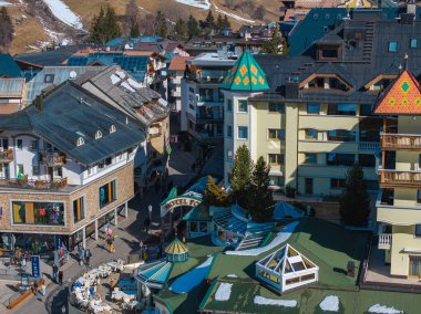 Yeşil çatısı ve kuleleri ile Hotel Post manzarası, renkli alp binaları, açık hava oturma ve Ischgl, Avusturya 'da kar tozlu tepeler ile çevrili.