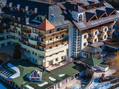 Avusturya 'nın Ischgl şehrinde çok katlı lüks bir otel, ahşap balkonlar, kırmızı üçgen bir bölüm, yeşil çatılı bir eklenti ve karlı çevresi var..