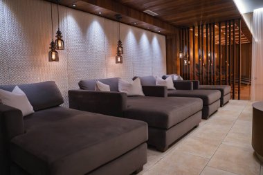 Koyu gri şezlonglar, beyaz yastıklar, kolye ışıkları, ahşap aksanlar, fayanslı döşemeler ve Avusturya 'nın Ischgl kentindeki yumuşak örtülerden oluşan sakin bir dinlenme odası..