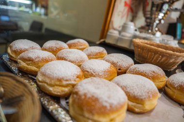 Beyaz seramik bardaklarla çevrili gümüş bir tepside toz şekere bulanmış taze fırınlanmış hamur işleri ve yumuşak ışıklandırmalı hasır bir sepet..