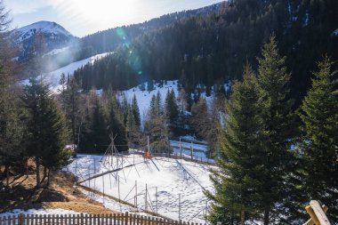 Karla kaplı yamaçlar, sık yeşil ormanlar, çitle çevrili çitlerle çevrili oyun alanı ve göze çarpan bir dağ zirvesi içeren sakin bir dağ manzarası..