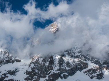 Matterhorn piramidi, engebeli, karla kaplı zirvelerin üzerinde yükselir, Alplerdeki parlak mavi gökyüzünün altında kısmen bulutlar tarafından gizlenir..
