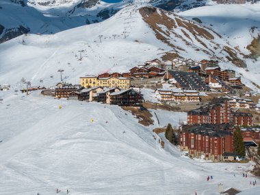 Dağ evi tarzı binaları, kayak asansörleri, yamaçları ve uzaktaki Matterhorn sıradağları olan karlı bir dağ kasabası. Kayakçılar ve snowboardcular görünür..
