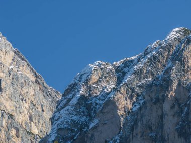 Dolomitler 'de açık mavi bir gökyüzüne karşı, dokusu kayalık yüzeyleri ve kar parçalarıyla engebeli, dik dağ tepelerinin yakın görüntüsü..