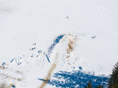 Kışın donmuş Braies Gölü 'nün hava görüntüsü, kar üzerinde lastik izleri, dağınık bireyler ve ağaç gölgeleri olan temiz bir yol gösteriyor..