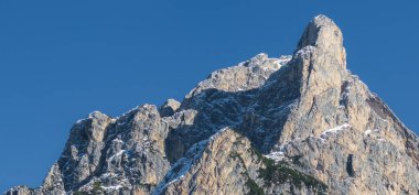 İtalya 'nın kuzeyindeki Dolomitler' de engebeli bir dağ zirvesi. Kayalık oluşumlar kısmen karla kaplı, açık mavi gökyüzüne karşı..