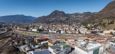 Bolzano, İtalya 'nın havadan görünüşü, bir tren istasyonu, teraslı üzüm bağları, modern ve geleneksel mimari ve uzaktan karlı zirveler.