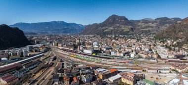 Bolzano, İtalya 'nın havadan görünüşü. Renkli trenleri, modern ve tarihi mimarisi ve arka planda Dolomite Dağları olan bir tren istasyonu..