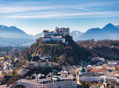 Avusturya 'nın Salzburg kentinin havadan görünüşü, bir tepedeki Hohensalzburg Kalesi, tarihi binalar, kiliseler ve açık gökyüzü altındaki kar kaplı Alpler..