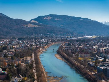 Salzburg, Avusturya 'nın hava manzarası, Salzach Nehri, bir köprü, ağaç çizgili yollar, kentsel binalar ve açık bir gökyüzünün altındaki orman dağları..