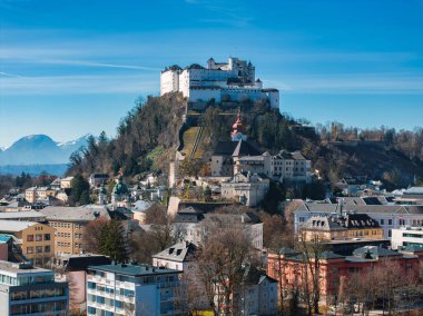 Avusturya 'nın Salzburg kentinin havadan görünüşü, Hohensalzburg Kalesi' nin bir tepe, tarihi binalar, kırmızı kubbeli bir kilise ve açık bir gökyüzü altındaki uzak dağlar..
