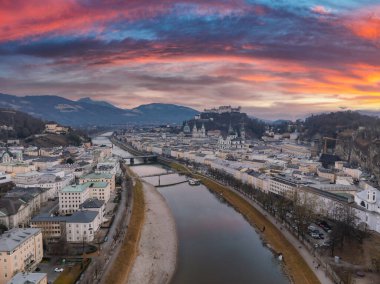 Salzburg, Avusturya 'nın havadan görünüşü, Salzach Nehri, Hohensalzburg Kalesi, tarihi mimari ve uzak dağların üzerinde canlı bir günbatımı..