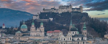 Salzburg, Avusturya 'nın havadan görünüşü, bir tepede Hohensalzburg Kalesi, yeşil kubbeli Salzburg Katedrali, tarihi çatılar ve günbatımı gökyüzü..