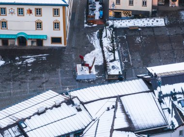 İtalya 'nın Cortina ve Ampezzo kentindeki bir meydanda kırmızı bir heykel, Alp tarzı binalar, kaldırım taşı kaldırımlar ve karla kaplı çatılar yer alıyor..