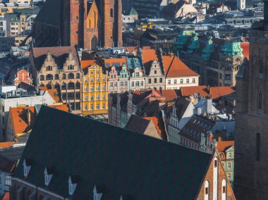 Wroclaw, Polonya 'nın canlı hava manzarası, renkli tarihi binalar, ikiz kuleleri olan gotik bir kilise ve ön planda koyu yeşil kiremitli bir çatı..