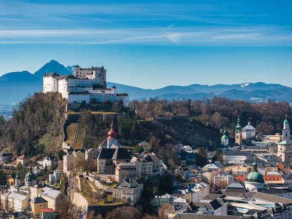 Avusturya 'nın Salzburg kentinin havadan görünüşü, bir tepedeki Hohensalzburg Kalesi, yeşil kubbeli tarihi kiliseler ve berrak gökyüzü altındaki uzak dağlar..