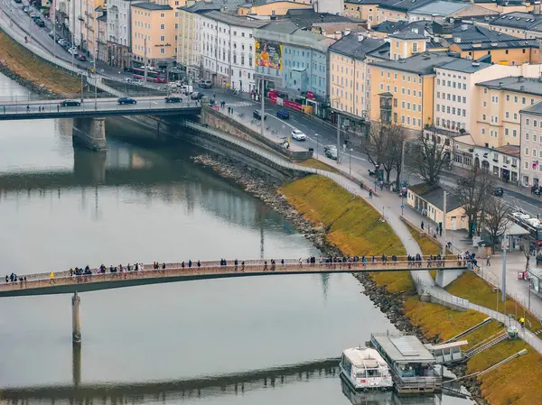 Salzburg, Avusturya 'nın havadan görünüşü, Salzach Nehri' ni, yaya köprüsünü, rıhtımlı bir tekneyi, tarihi binaları, bir duvar resmini ve çevresindeki yeşillikleri gösteriyor..