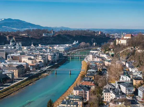 Salzburg, Avusturya hava manzarası, Salzach Nehri, tarihi binalar, yaya köprüsü, Hohensalzburg Kalesi ve uzak dağlar.