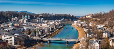Salzburg, Avusturya 'nın hava manzarasında Salzach Nehri, Salzburg Katedrali, Hohensalzburg Kalesi, köprüler ve etrafındaki tepeler berrak gökyüzü altındadır..
