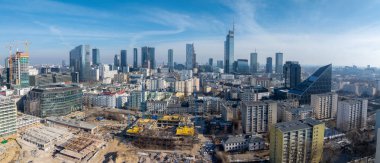 Varşova, Polonya 'nın havadan görünüşü, Varso Kulesi, inşaat alanları, yükselen binaların ortası, ve temiz bir gökyüzü altında üçgen camdan çatılar..