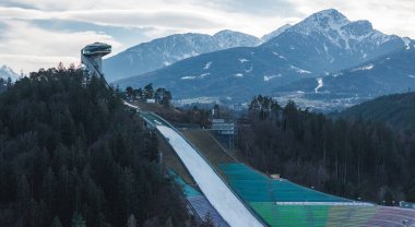 Innsbruck, Avusturya 'da Bergisel Kayak Atlayışı, modern kulesi, dik rampası, renkli koltukları ve arka planda kar kaplı Alp dağlarıyla.