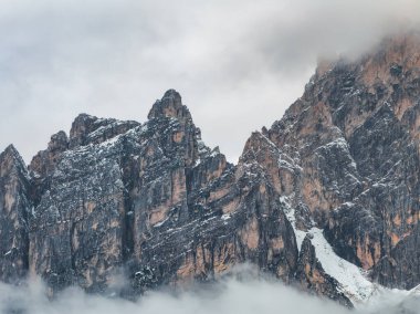 İtalya, Cortina yakınlarındaki engebeli Dolomite dağ zirveleri, keskin hatları, kar tozlu uçurumları, alçak asılı bulutlar, dramatik ışık ve gölgeler.