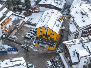 Alp mimarisi ve karlı çatılarla çevrili, eğimli ve kemerli pencereli parlak sarı bir binanın bulunduğu Cortina, İtalya 'nın hava manzarası..