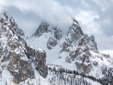 İtalya 'nın Cortina yakınlarındaki Dolomite tepeleri kar altında kısmen bulutlarla örtülüydü. İnce kozalaklı ağaçlar, engebeli araziye zıt olarak, alçak yamaçları nokta.