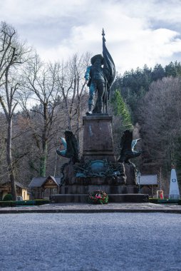 Avusturya 'nın Innsbruck kentindeki yapraksız ağaçlar ve anıtsal unsurlarla çevrili, heykel oyulmuş kartallarla dolu bir kaidede, elinde bayrak tutan tarihi bir figürün heykeli duruyor.