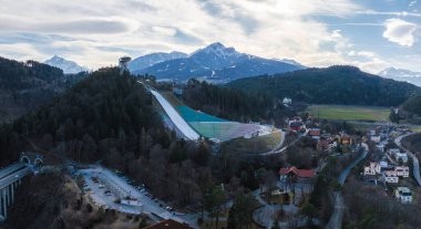 Avusturya 'nın Innsbruck kentindeki Bergisel Kayak Atlayışı' nın havadan görünüşü. Ormanlar, yerleşim alanları ve arka planda Alpler ile çevrili açık alanlar..