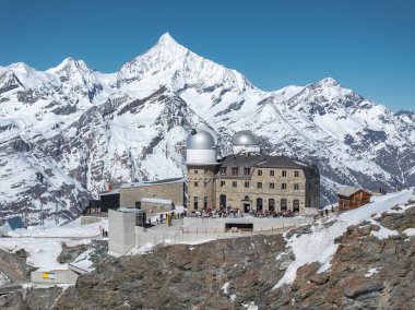 Gornergrat Gözlemevi. Kayalık bir yamaçta gümüş kubbeler. Karlı tepelerle çevrili..