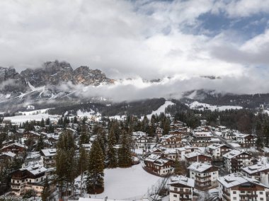 İtalya 'daki Cortina ve Ampezzo' nun havadan görünüşü, karla kaplı çatılar, yemyeşil ağaçlar, kayak yamaçları ve Dolomitlerin dramatik zirveleri.
