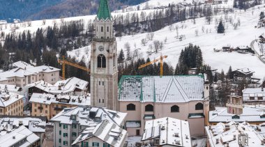 Dolomitlerdeki Cortina ve Ampezzo 'nun hava manzarası, Basilica Minore dei Santi Filippo ve Giacomo' nun yer aldığı, karla kaplı çatılar ve inşaat vinçleri..