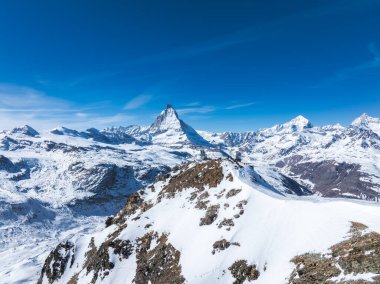 Kar, Matterhorn dağını kayalık bir tepe, küçük bir gözlemevi ve İsviçre 'nin Zermatt kenti yakınlarında açık mavi bir gökyüzünün altında çevreleyen dağlarla kapladı..