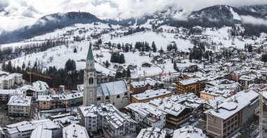 İtalya 'nın Cortina dAmpezzo kentinin havadan görünüşü, Basilica Minore dei Santi Filippo ve Giacomo' nun yer aldığı, karla kaplı çatılar ve sisli Dolomite tepeleri.