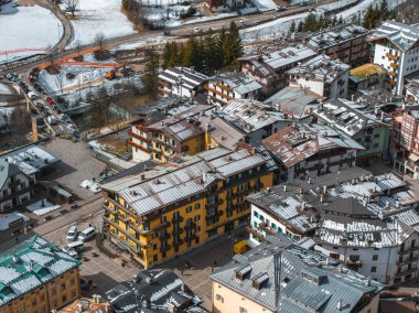 İtalya, Dolomitlerdeki Cortina dAmpezzo 'nun hava görüntüsü renkli binalar, karla kaplı tarlalar, dolambaçlı bir yol ve görünür inşaat faaliyetlerini gösteriyor..