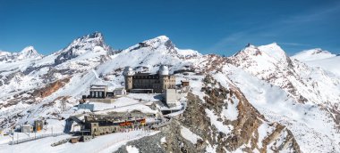 İkiz kubbeleri, karlı tepeleri, Matterhorn 'u, tren istasyonunu, turuncu treni, ziyaretçileri ve açık mavi gökyüzünü gösteren Gornergrat Gözlemevi' nin hava manzarası..