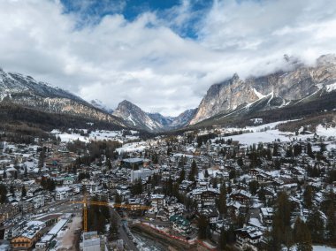 İtalya 'nın Cortina dAmpezzo kentinin havadan görünüşü karlı çatıları, engebeli Dolomite tepelerini ve bulutlu bir gökyüzünün altındaki inşaat alanını gösteriyor..