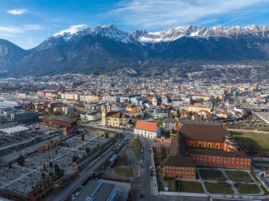 Innsbruck, Avusturya 'nın hava manzarası, Nordkette dağları, tarihi ve modern mimari, kırmızı çatılı bir bina, ve bir mezarlık..