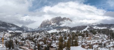 İtalya 'da kar kaplı çatılar, yemyeşil ağaçlar, Dolomitler, alçak bulutlar ve görünür bir vinç ile Cortina dAmpezzo' nun hava görüntüsü.