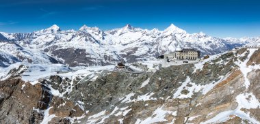 İsviçre Alpleri 'nin arka planında Matterhorn ve İsviçre' nin Zermatt kenti yakınlarındaki açık mavi gökyüzünün altında kayalık bir sırt üzerindeki Gornergrat Gözlemevi karla kaplıydı..