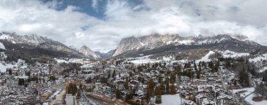 İtalya 'nın Cortina dAmpezzo kentinin hava manzarası karlı dağları, çatıları, dolambaçlı sokakları ve 2026 Kış Olimpiyatları için bir inşaat alanını gösteriyor..