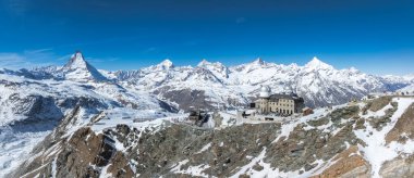 Kar İsviçre Alplerini solda Matterhorn, önde Gornergrat Gözlemevi, kayak pistleri ve açık mavi gökyüzü altında ziyaretçiler kapladı.