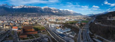 Avusturya 'nın Innsbruck kentinin havadan görünüşü, kırmızı çatılı binalar, önemli bir kilise, yollar, demiryolları ve karla kaplı Nordkette sıradağları.