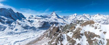 İsviçre Alpleri karla kaplıydı. Matterhorn zirvesi merkezde, Gornergrat Gözlemevi kayalık bir tepede ve açık mavi gökyüzü alp arazisini aydınlatıyordu..