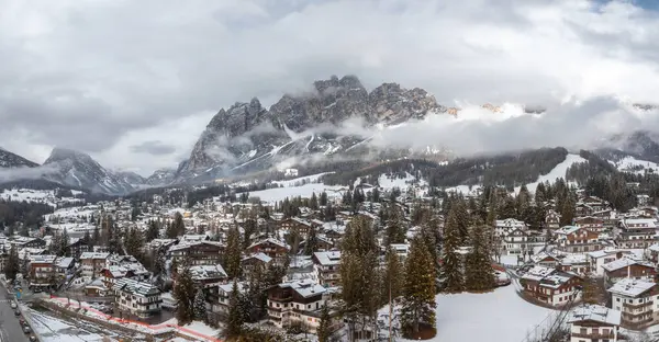İtalya 'daki Cortina dAmpezzo' nun havadan görünüşü, karla kaplı çatılar, dağlık binalar, yemyeşil ağaçlar ve Dolomitler kısmen bulutlarda zirve yapıyor..